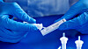 closeup of a male healthcare worker, wearing blue surgical gloves, placing the sample into the covid-19 antigen diagnostic test device, on a blue table