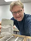 Geolog i Equinor, Dirk Knaust, viser frem steinprøven med beinbiten i. Beinet er fra en fiskeøgle kalt ichthyosaur. Foto: Privat