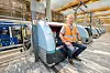 Per Viggo Andersen, fagleder for bagasje ved Oslo lufthavn, sitter på en av de siste ti selvbetjente bagasjedropboksene som er under installasjon på Oslo lufthavn. Når bagasjen legges inn i boksen, plasseres den på en plastkasse og sendes ned til etasjen under med heisen som ses til venstre. Foto: Arash A. Nejad
