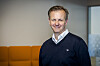 Portrett av Fredrik Witte i mørk genser foran en oransje sofa på et kontor.