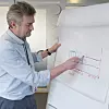 Stig Tjøtta illustrerer hvordan ekstruderte profiler vil bli lagt rundt batteriet for å beskytte det mot kollsionsskader. Foto: Joachim Seehusen