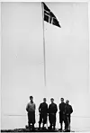 Flaggheising i Myggbukta ved okkupasjonen av Eirik Raudes Land 27. juni 1931. Til venstre er lederen for ekspedisjonen, Hallvard Devold. Foto: Hallvard Devold/Norsk Polarinstitutt