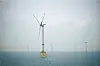 En havvindturbine med gul konstruksjon står i gråblått hav, med flere turbiner synlige i tåken.