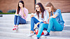 Modern teen girls with cellphones sitting on stairs on background of reading student