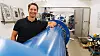 Kristoffer Aune Brekken i ved testriggen NTNU er alene om. Det er nærmest som et overdimensjonert luftgevær, med 20 meter langt løp. I bakgrunnen resultatet fra tidligere tester.