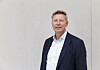 Portrett av Egil Thompson i mørk dress foran en lys vegg.