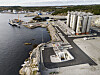 Flyfoto av et kystnært industrianlegg med store lagringstanker, rør, kai og skip.