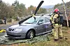 Brannmann i verneutstyr undersøker en skadet personbil i skogsterreng.