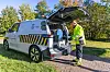 Feltarbeider i verneklær ved en blå og gul servicebil med bakluken åpen.
