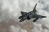 Et fransk Mirage 2000D-fly i lav vinkel over skyer og et tørt landskap.