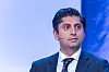 Himanshu Gulati i mørk dress og slips står foran en blå bakgrunn og snakker med headsetmikrofon.