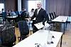 Mann i mørk dress står foran et møtebord og holder en presentasjon i et konferanserom.