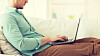 technology, home and lifestyle concept - close up of man working with laptop computer and sitting on sofa at home