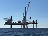 Små hjelpere: Installasjonsskipet Brave Tern assisteres av tre små amerikanske jackup-fartøy, hver med tre ben (til høyre), som leverer vindturbin-deler til installasjonsfartøyet. Her løftes nacellen (generatoren) til den første vindmøllen. Foto: Deepwater Wind